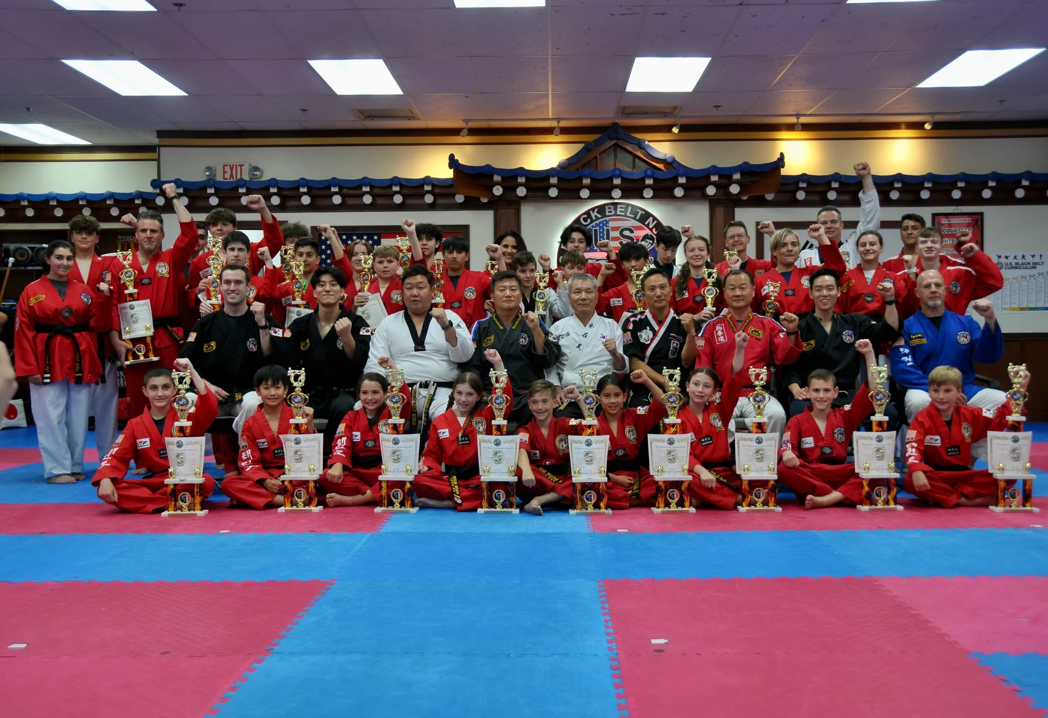 A large competition team in red uniforms poses with their trophies on the mat